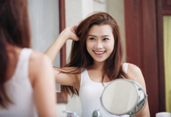 Attractive smiling young woman looking at herself in mirror